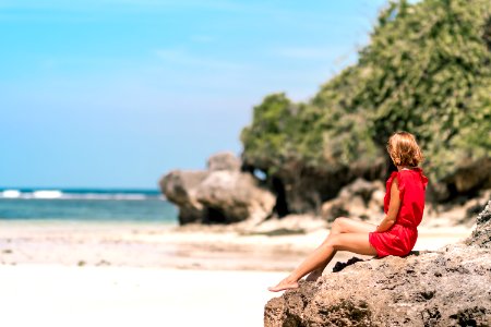 Woman In Red Dress Sitting On Brown Rock photo