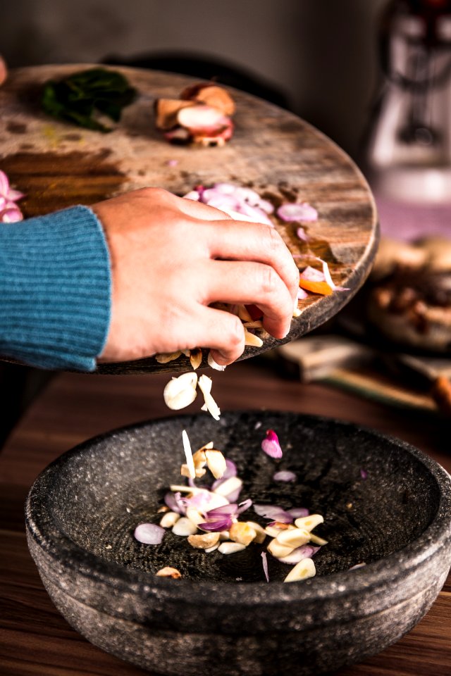 Person Pouring Sliced Spices From A Chopping Board To Black Bowl