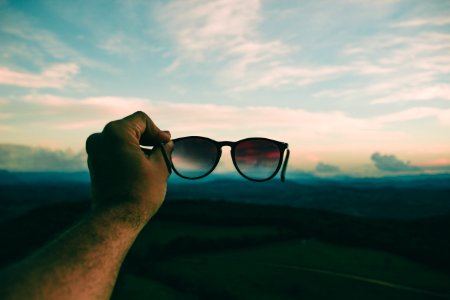 Person Holding Black Framed Sunglasses Under Blue Sky And White Clouds