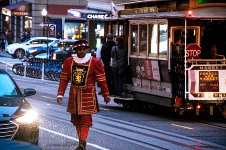 Man Wearing Red And Yellow Dress Walking On Concrete Road Near White And Red Cable Train photo