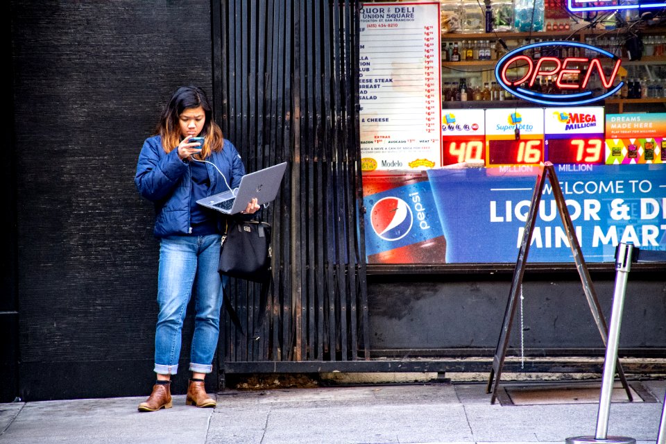 Woman In Blue Jeans Holding Macbook Pro Standing Against Black Wall