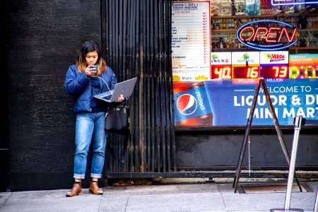 Woman In Blue Jeans Holding Macbook Pro Standing Against Black Wall photo
