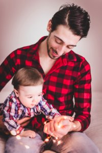 Man Wearing Red And Black Gingham Sports Shirt With Baby Beside Him photo