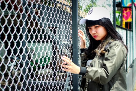 Woman Wearing Grey Bomber Jacket Leaning Near Grey Wire Fence