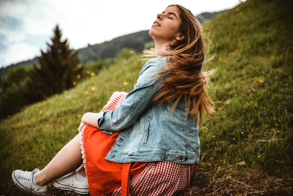 Woman Wearing Blue Denim Jacket Sitting On Green Grass Near Trees Under Blue Sky At Daytime