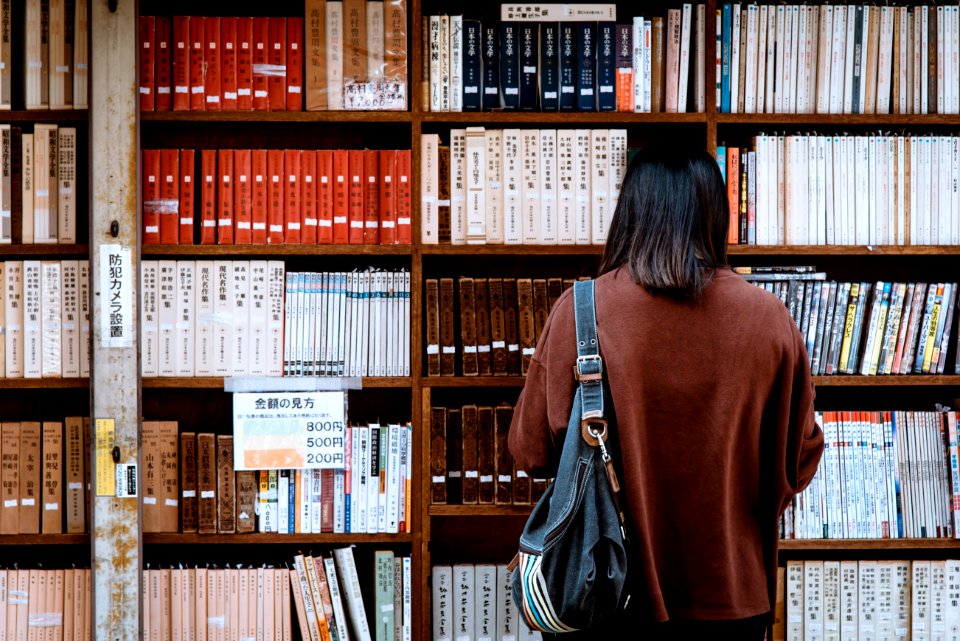 Woman Wearing Brown Shirt Carrying Black Leather Bag On Front Of Library Books
