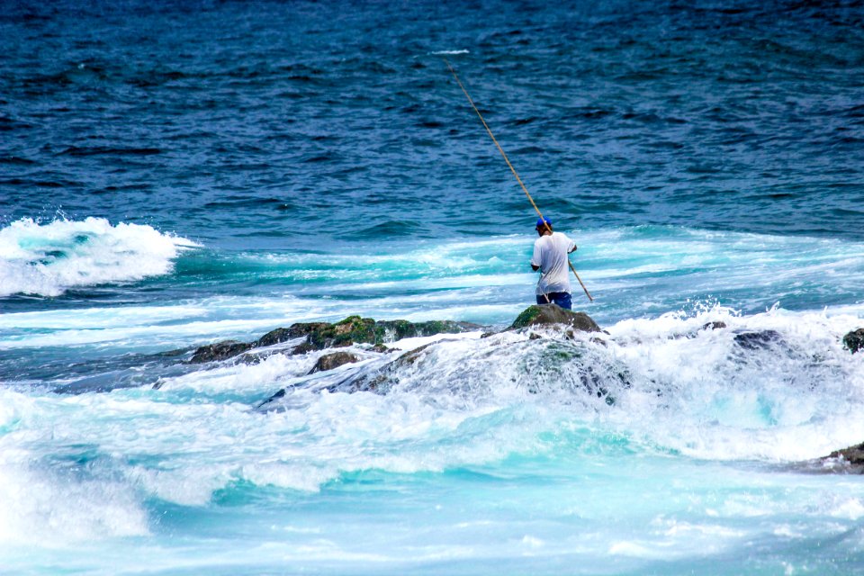 Man In White Shirt Holding A Fishing Rod While Standing On Rock
