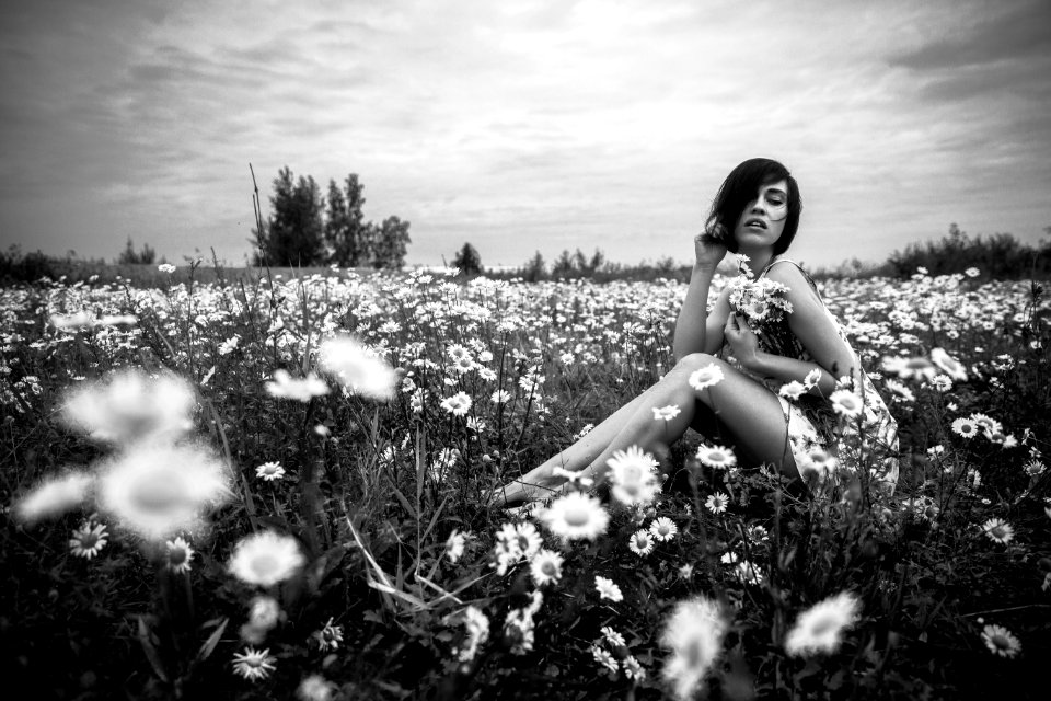 Grayscale Photo Of Woman Sitting Beside Daisies