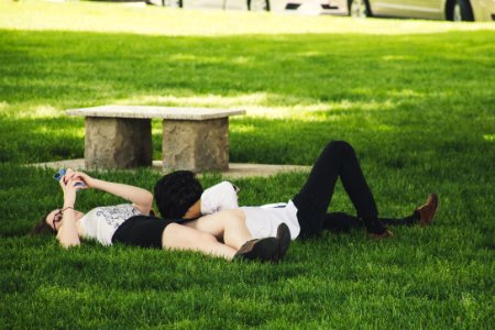 Man And Woman Laying On Green Grass Near Concrete Bench photo