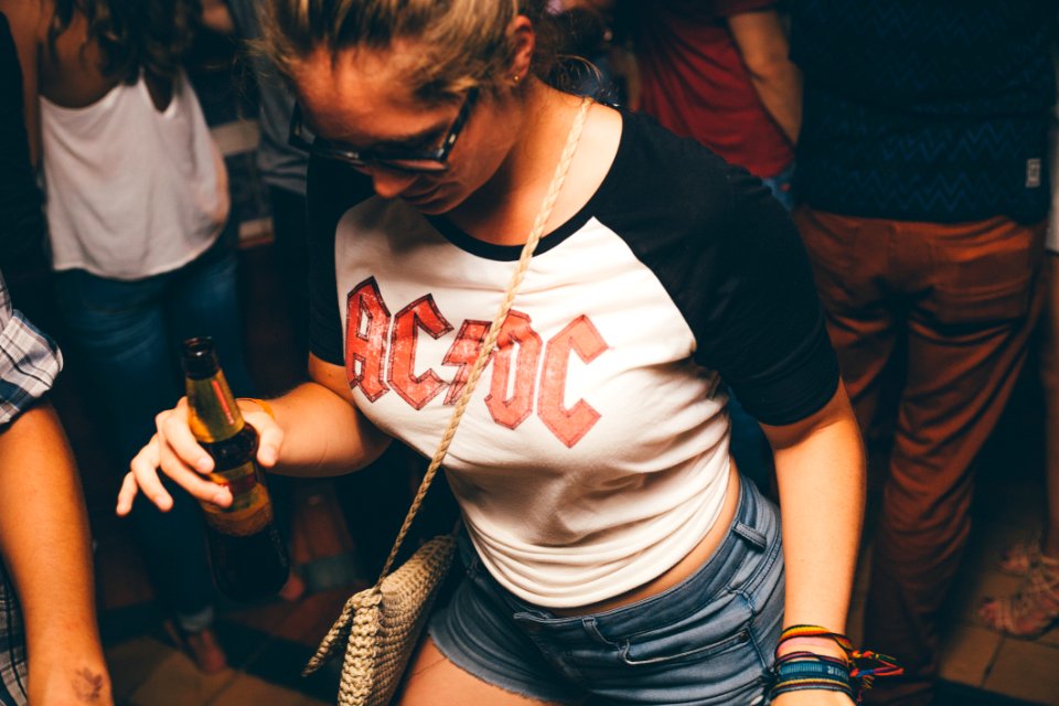 Woman Wearing White And Black Shirt With Acdc Print Holding Brown Glass Bottle