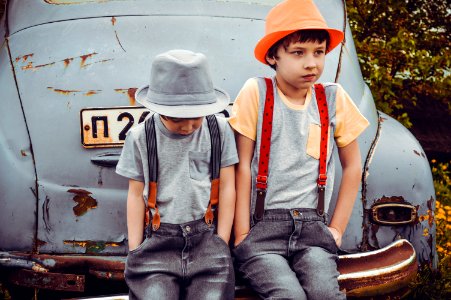 Two Boys Wearing Gray Shirts Sitting On Gray Vehicle Bumper photo