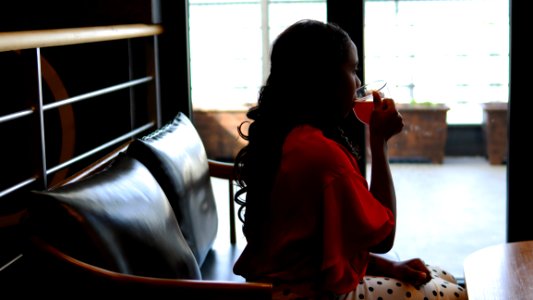Woman Wearing Red Long-sleeved Blouse Sitting And Drinking Liquid photo