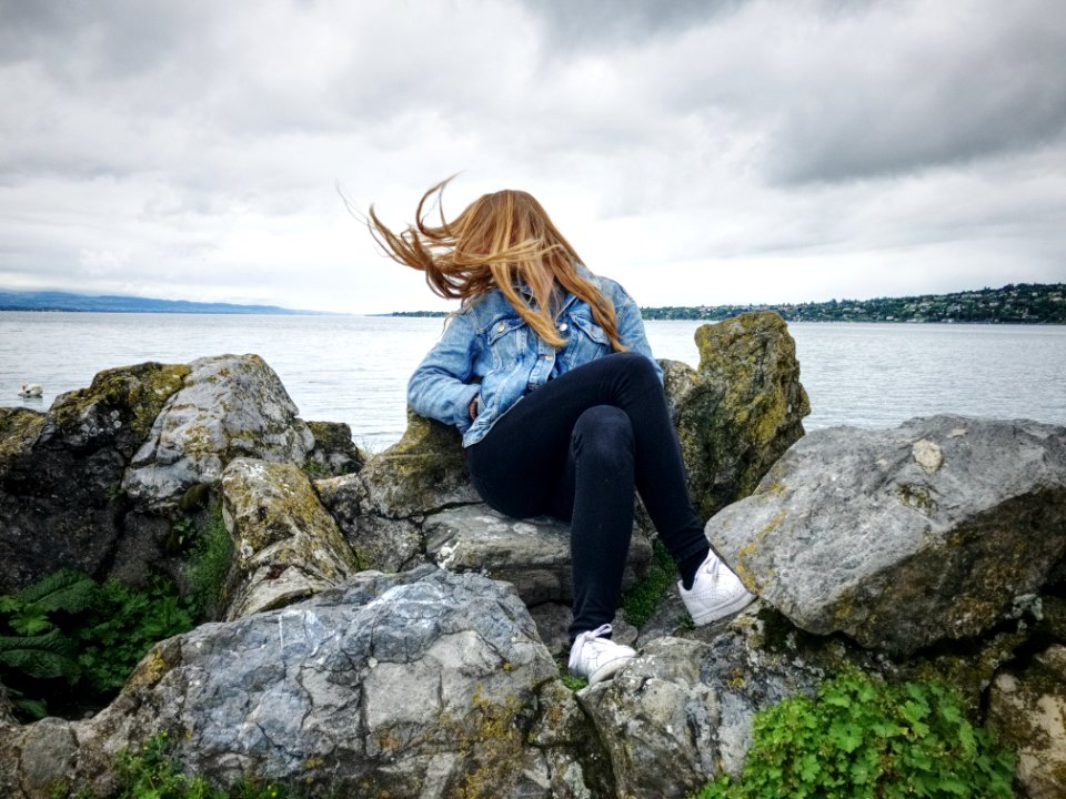 Woman With Blue Denim Collared Button-up Jacket And Black Jeans Sitting On Gray Rock Watching Lakeview