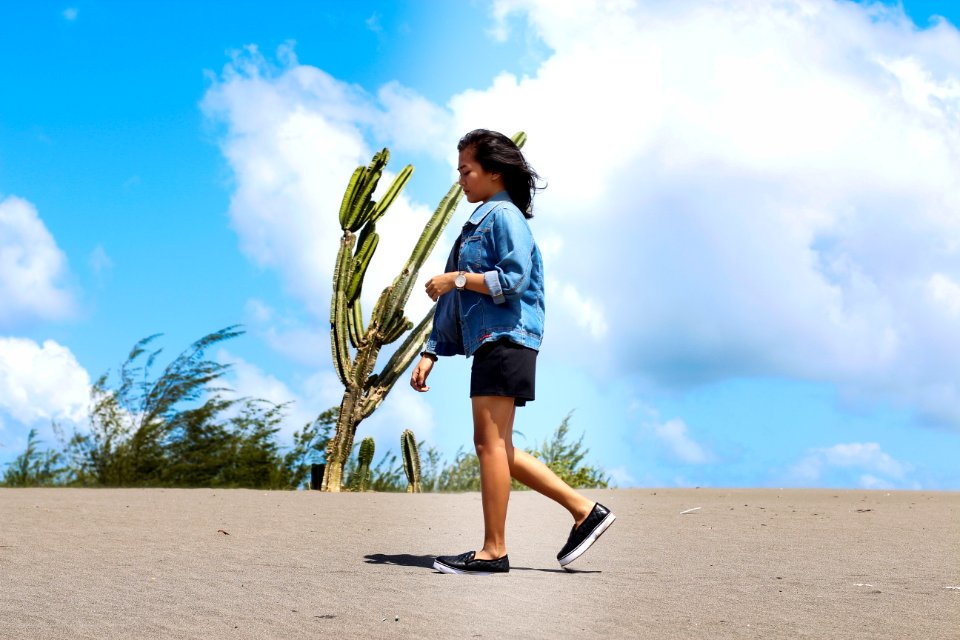 Woman Wearing Chambray Jacket And Black Shorts Walking On Sand Near A Cactus At Daytime
