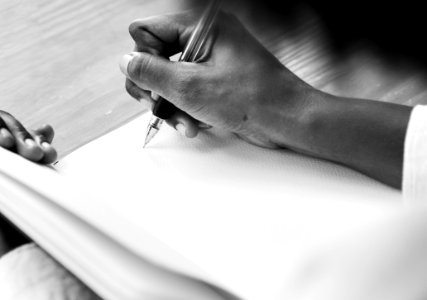 Grayscale Photography Of A Person Holding Ball Point Pen Writing On White Notebook Page