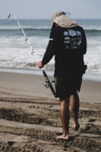 Man In Black Long-sleeved Top Holding White Fishing Rod Near Beach photo