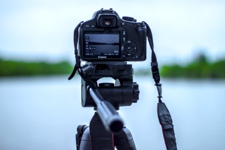 Selective Focus Photo Of Black Canon Camera On Tripod Stand In Front Of Body Of Water Photo photo