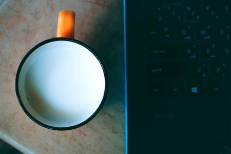 Orange And Black Ceramic Mug With Milk Beside Black Laptop photo