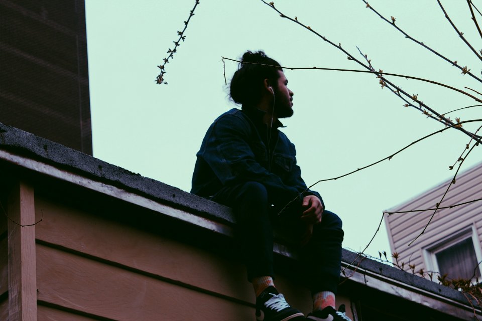 Man Wearing Black Jacket With Black Pants Sitting On Roof At Daytime