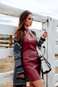 Woman Wearing Maroon Leather Dress And Cardigan Leaning On White Plank Wall photo