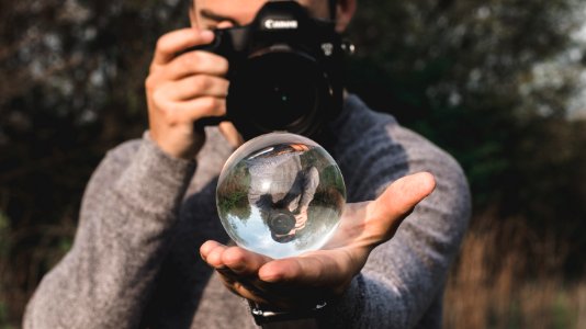 Man Wearing Space-dyed Sweater Holding Water Globe While Holding Black Canon Camera photo