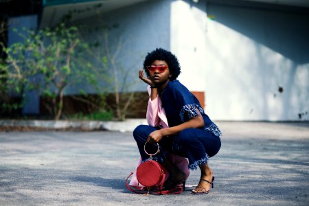 Woman Wearing Blue Shirt And Pants Holding Red Leather Barrel Bag photo
