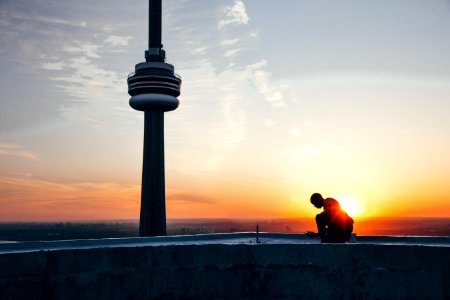 Silhouette Of A Man Sitting Near Black Tower Near Body Of Water During Sunset photo
