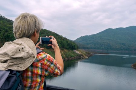 Person Holding Smartphone While Taking Photo Of Calm Water Near Mountain At Daytime photo
