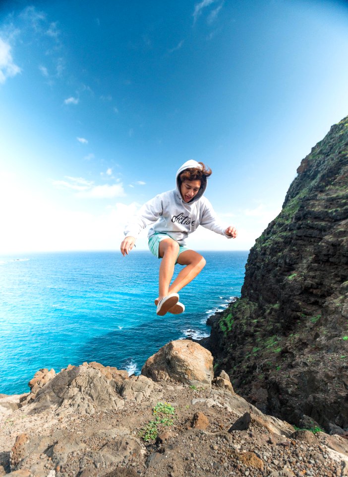 Man Wearing Gray Hoodie Jumping At Rock photo