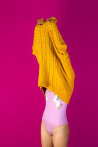 Photo Of Woman About To Wear Off Yellow Sweater In Pink Background photo