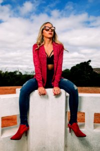 Woman Wearing Red Jacket And Distressed Blue Denim Skinny Jeans Sitting On Bench photo