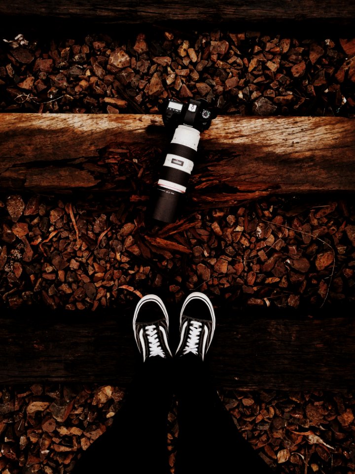 Person Wears Black-and-white Vans Low-top Sneakers Stands In Front Of Black Dslr Camera