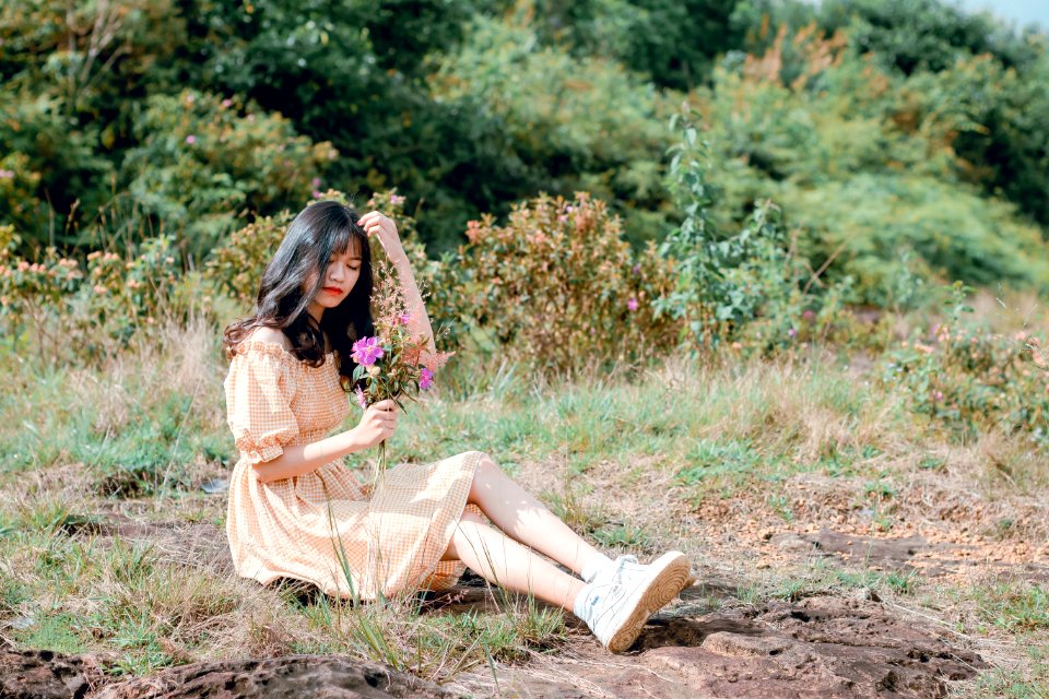Woman Wearing Brown Dress Sitting On Grasses While Holding Purple Flowers