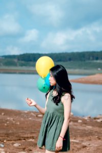 Woman In Green Crew-neck Sleeveless Mini Dress Holding Balloons Near Body Of Water photo