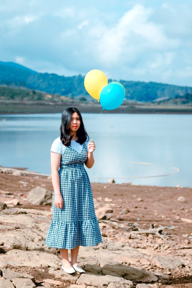 Woman In White And Black Dress Stands While Holding Party Balloons