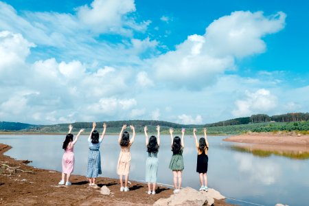Six Girls Raise Their Hands In Front Of Body Of Water photo