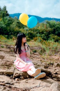 Woman Wearing Pink Dress Sitting On Ground Holding Two Balloons photo