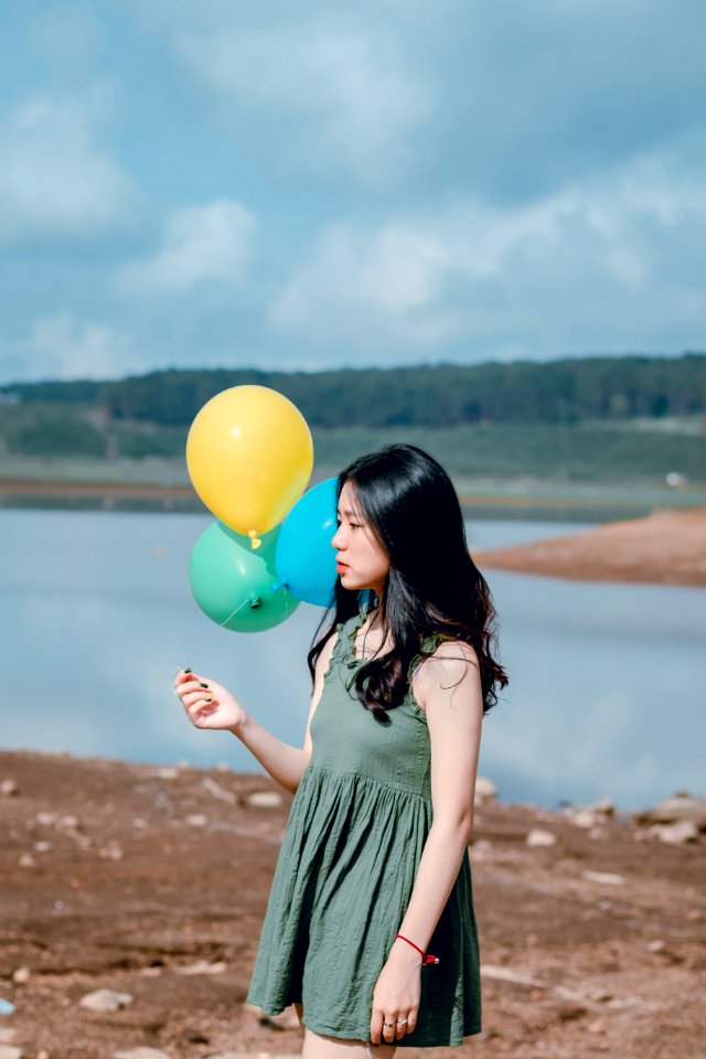 Woman In Green Sleeveless Dress Holding Yellow Green And Blue Balloons