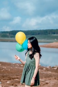 Woman In Green Sleeveless Dress Holding Yellow Green And Blue Balloons photo