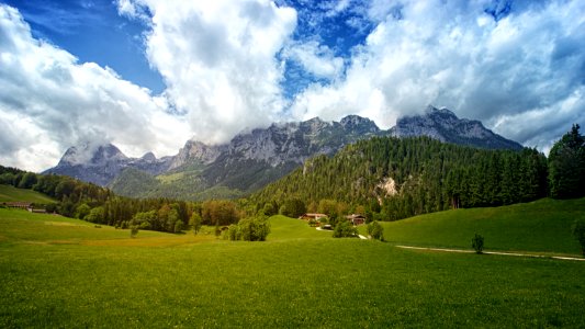 Green Grass Field With Trees And Mountain In Background Under Cloudy Sky photo