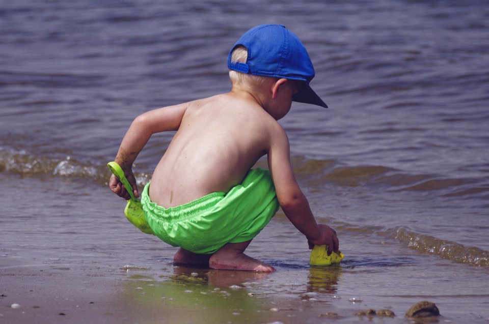 Boy In Blue Cap And Green Shorts Playing On Seashore