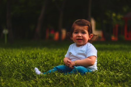 Girl Wearing White T-shirt And Blue Pants Sitting On Green Grass photo