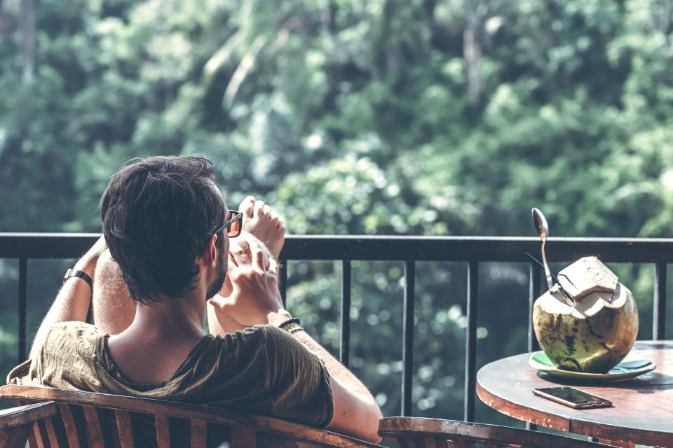 Man Sitting On Wooden Chair With Foot On Black Steel Railings