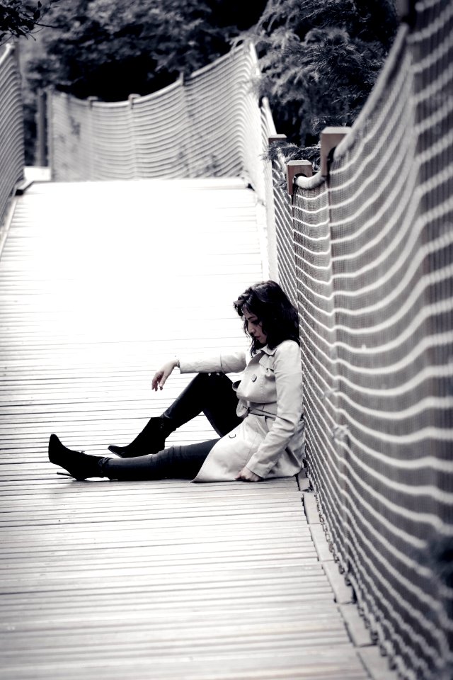 Low Light Photo Of Woman Wearing Trench Coat Sitting Against Wall