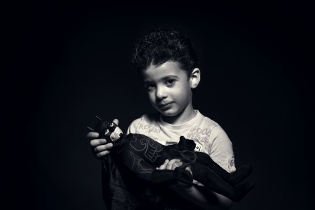 Grayscale Photo Of A Boy Holding Batman Plush Toy