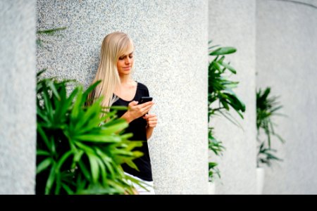Woman Wearing Black Scoop-neck Shirt Standing In Front On Concrete Column Holding Smartphone photo