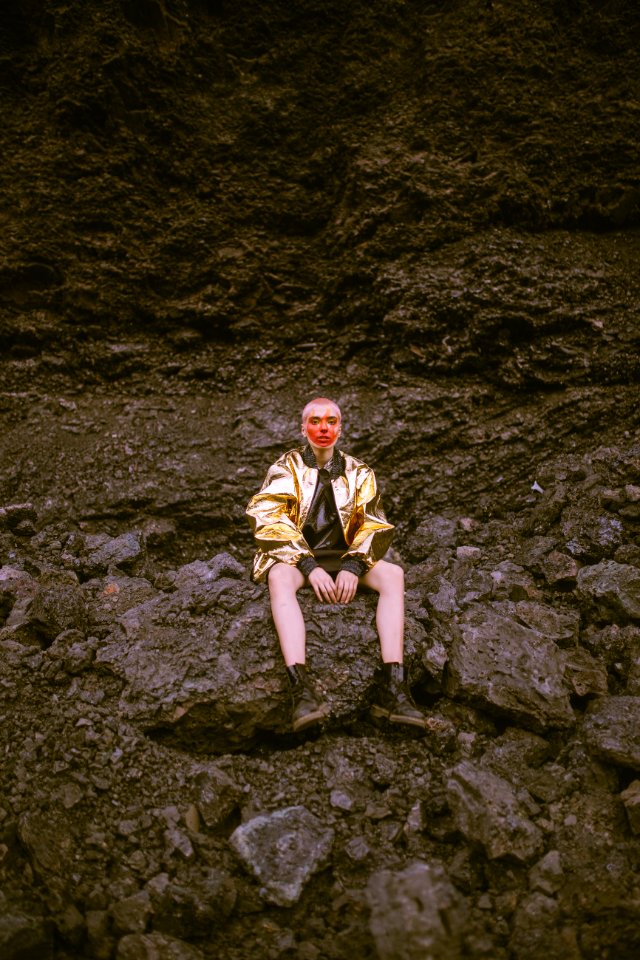 Man Wearing Gold Jacket Sitting On Stone