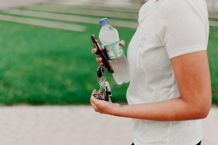 Person Holding Key Smartphone And Plastic Bottle photo