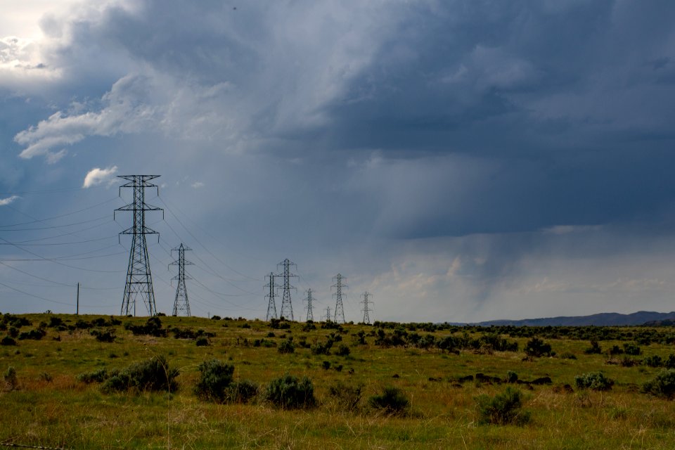 Gray Electric Post On Green Field Under White Clouds And Blue Sky