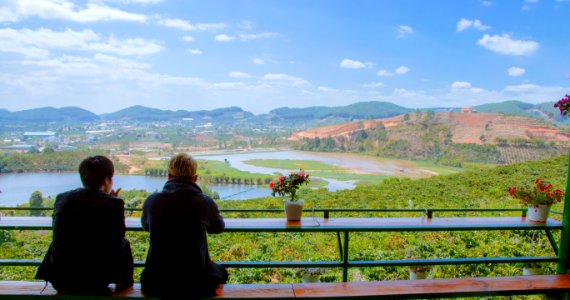 Two Men Sitting On Table Facing Lake